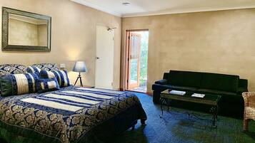 Ein Schlafzimmer mit einem großen Bett, einem grünen Sofa, einem kleinen Tisch und einer Tür, die auf einen Balkon führt.
