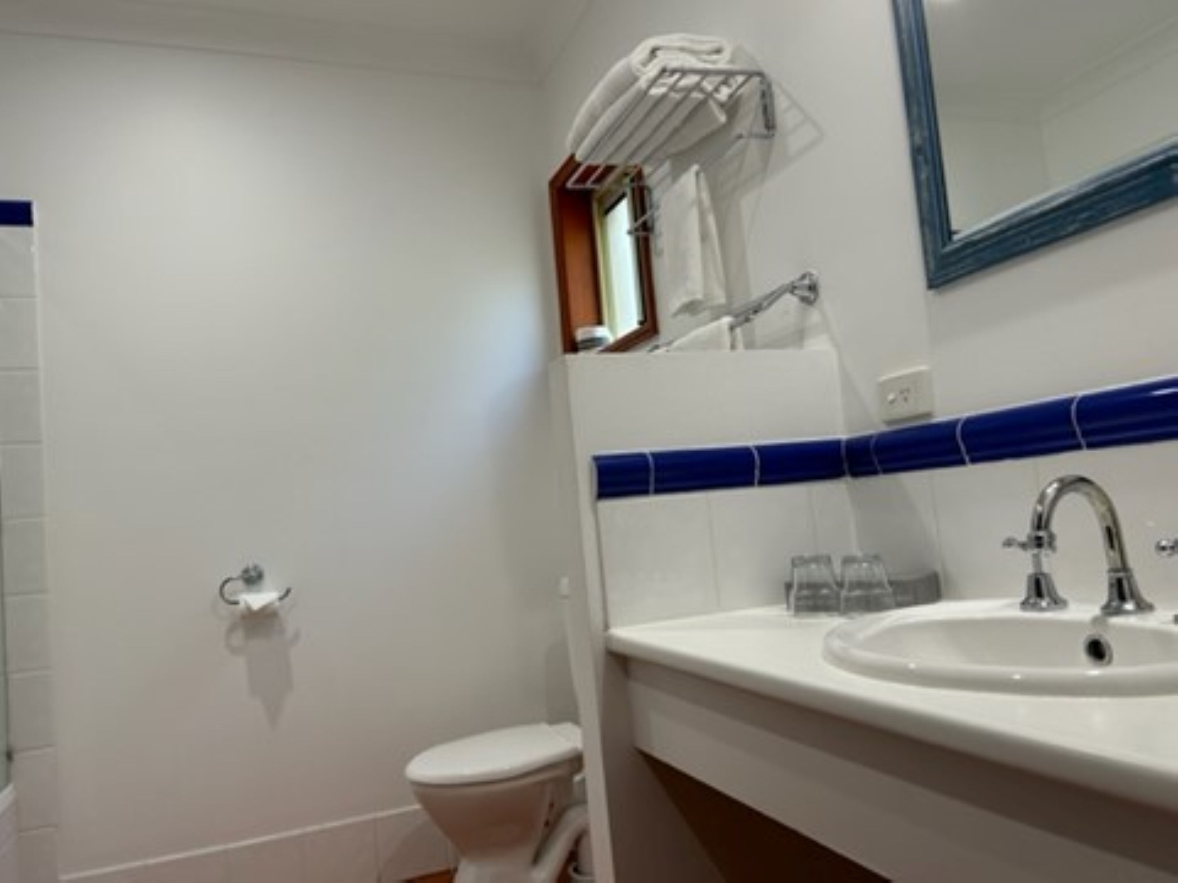 Une salle de bain avec des toilettes blanches, un lavabo doté d’un plan-vasque recouvert de carreaux bleus et un miroir au-dessus du lavabo.