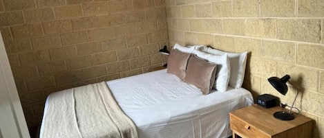 A bedroom with a bed, a bedside table, a lamp, and a brick wall.