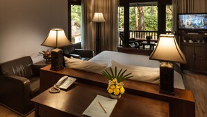 Quarto de hotel com cama, mesa de escritório, telefone, bloco de notas, abajur e televisão em um suporte.