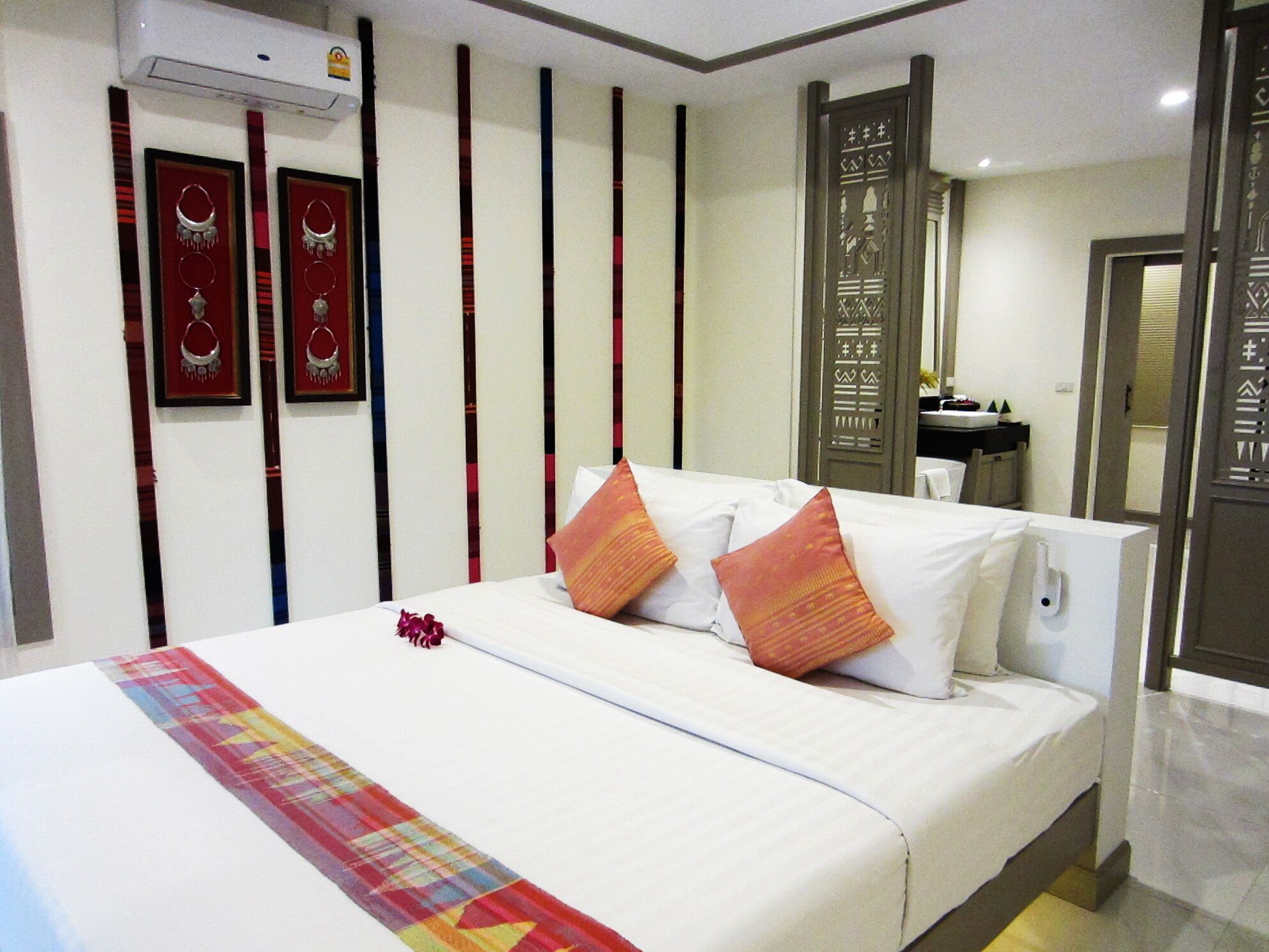 A hotel room with a bed, a bedside table, a mirror, and a wall with vertical stripes and framed pictures.