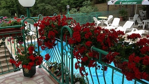 Un espace piscine agrémenté de fleurs rouges, de chaises longues blanches et d’une clôture verte.