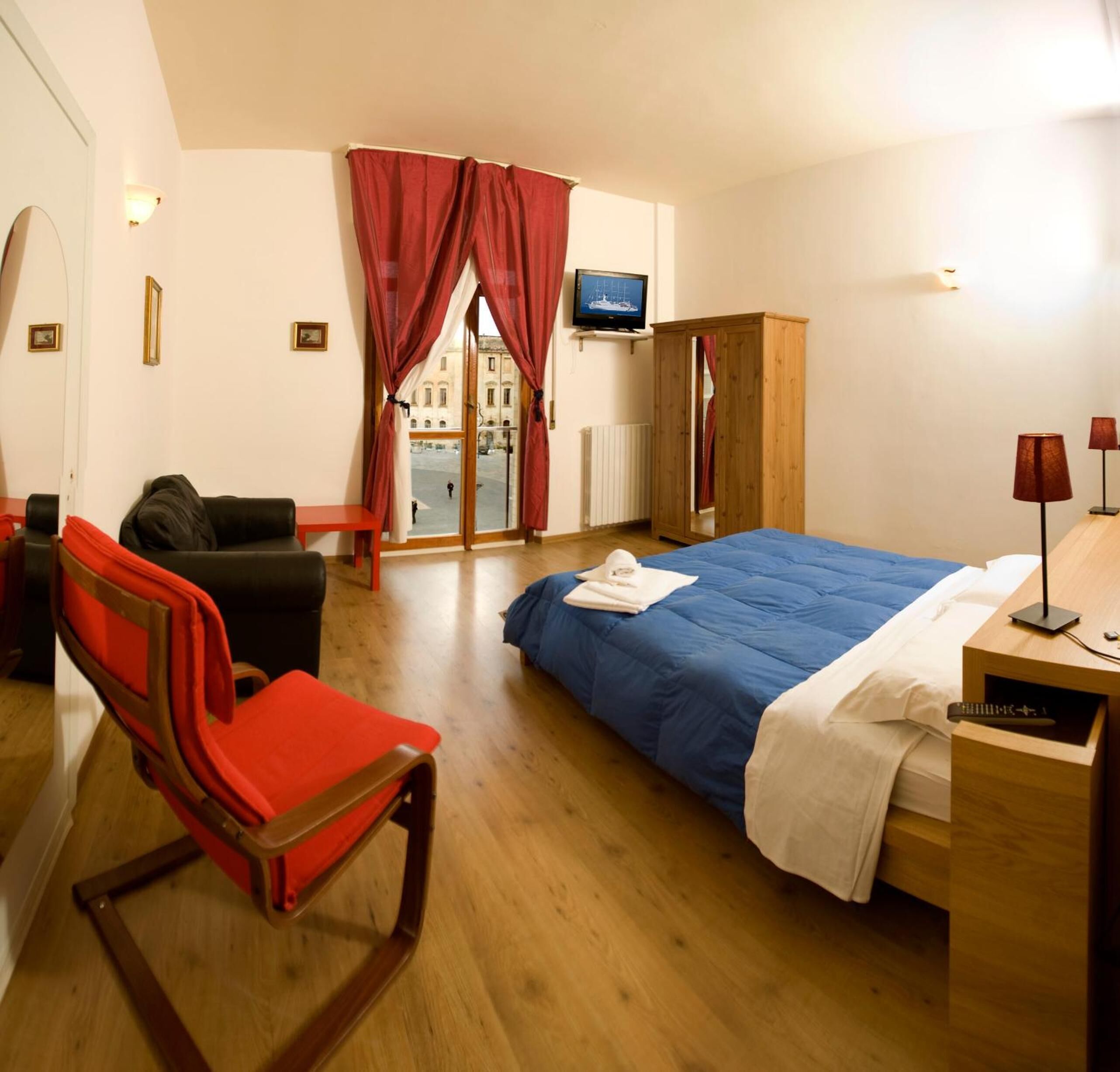 A hotel room with a bed, a chair, a TV, and a view of the street.