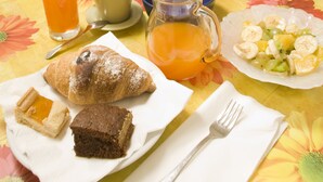 Et morgenbord med en croissant, et stykke kage, et glas appelsinjuice, en tekedel, en kande appelsinjuice og en bakke med frugt.