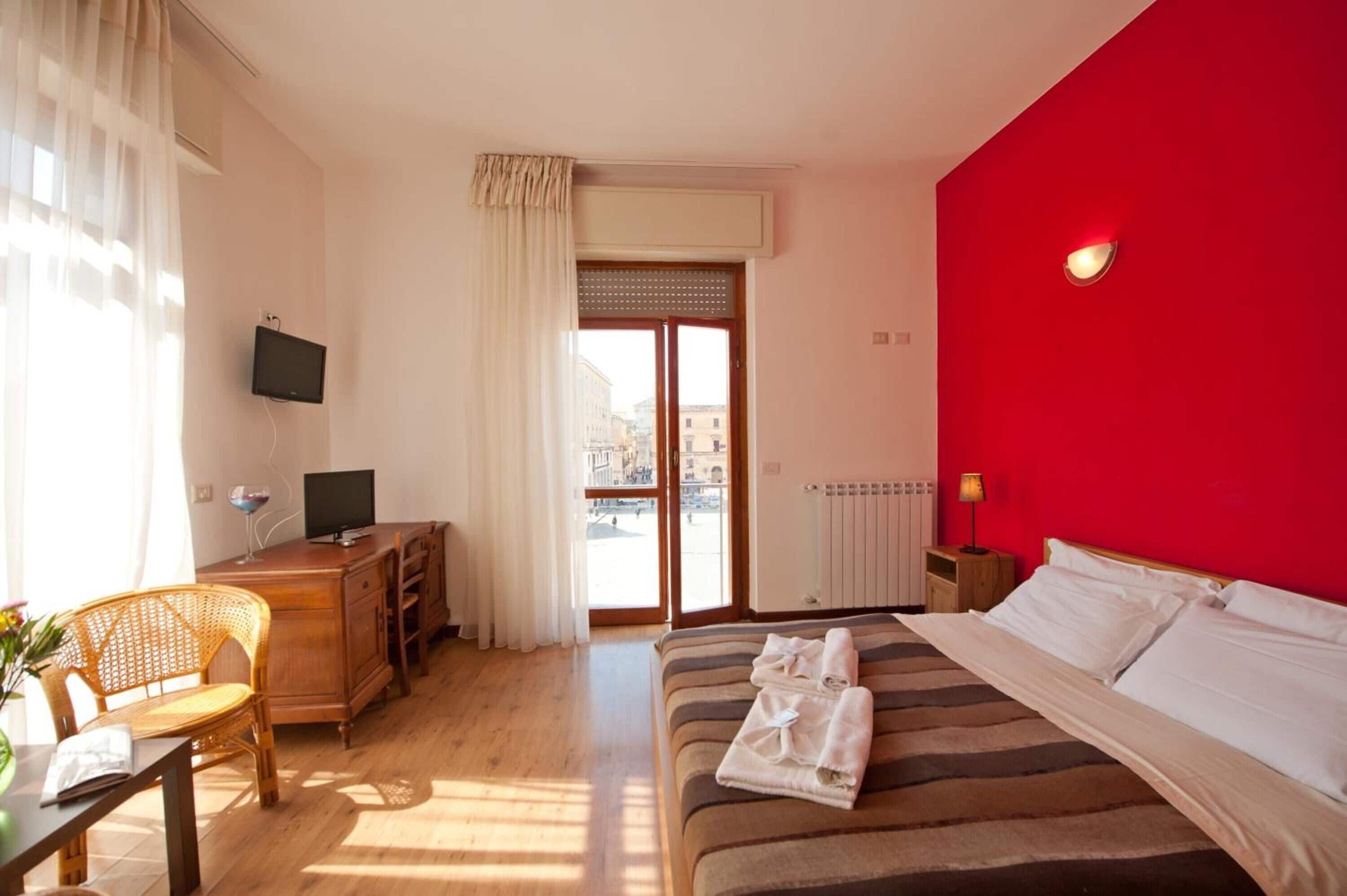 A hotel room with a bed, a desk, a chair, a TV, and a window with curtains.