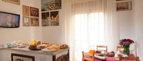 A dining area with a table set for breakfast, including pastries and a vase of flowers.