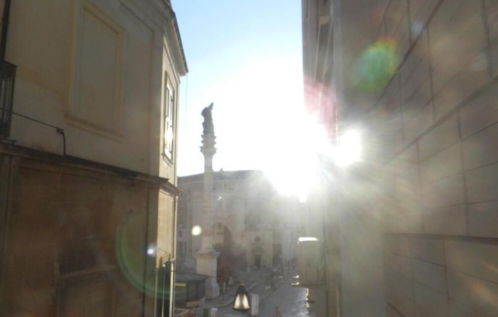 Une rue étroite, bordée de bâtiments des deux côtés, un lampadaire et une statue au loin.
