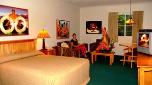 A hotel room with a large bed, a sofa, a small table, a TV, and artwork on the walls. - Sadie Thompson Inn (Pago Pago)