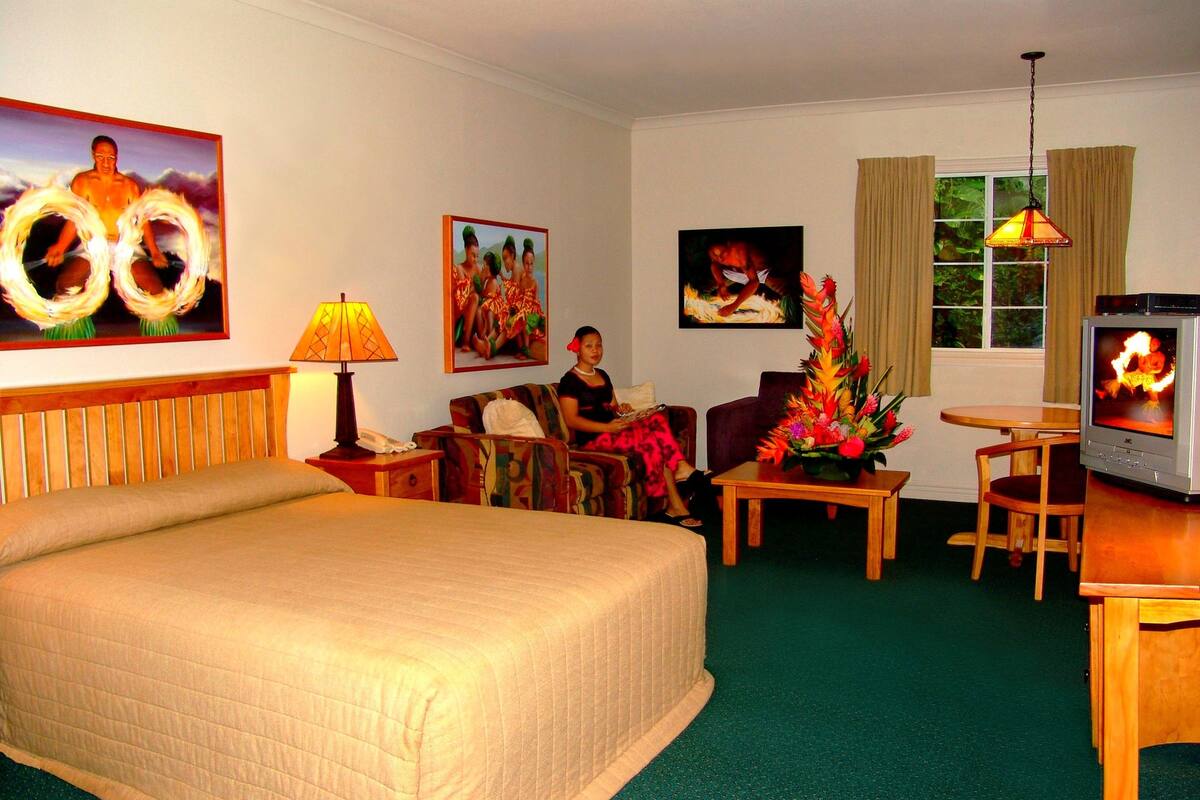 A hotel room with a large bed, a sofa, a small table, a TV, and artwork on the walls.