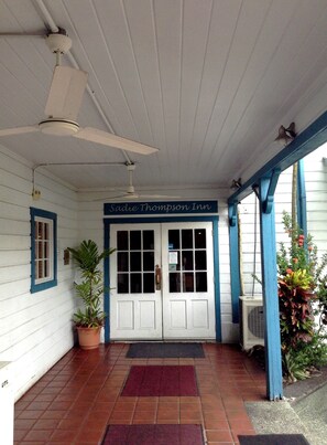 A building entrance with a sign reading "Sadie Thompson Inn," a tiled porch, a ceiling fan, and a potted plant.