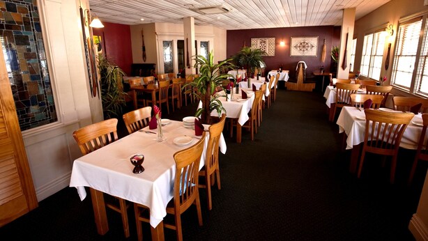 A restaurant with multiple tables and chairs, white tablecloths, and potted plants. - Sadie Thompson Inn (Pago Pago)