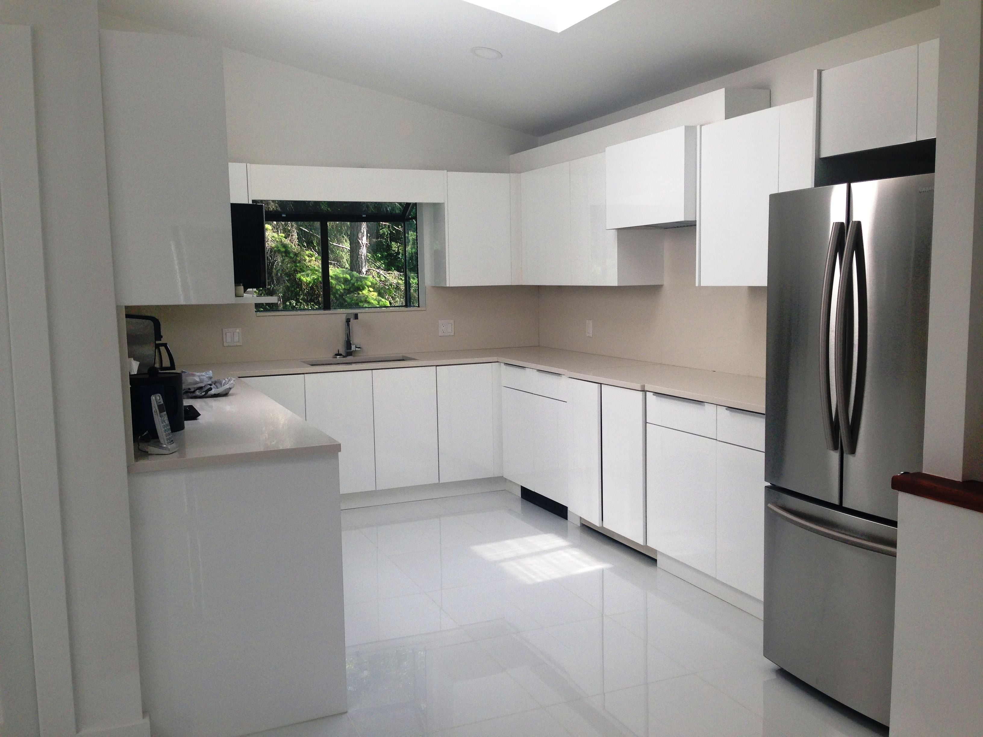 Una cocina moderna con armarios blancos, un refrigerador de acero inoxidable y una ventana con vistas a la vegetación.