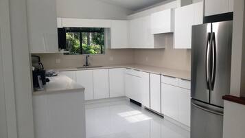Una cocina moderna con armarios blancos, un refrigerador de acero inoxidable y una ventana con vistas a la vegetación.