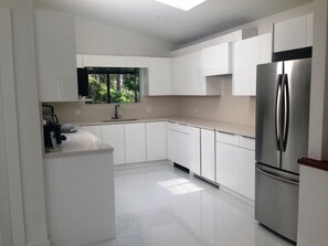 A modern kitchen with white cabinets, a stainless steel refrigerator, and a window with a view of greenery. - Rockwater Secret Cove Resort (Halfmoon Bay)