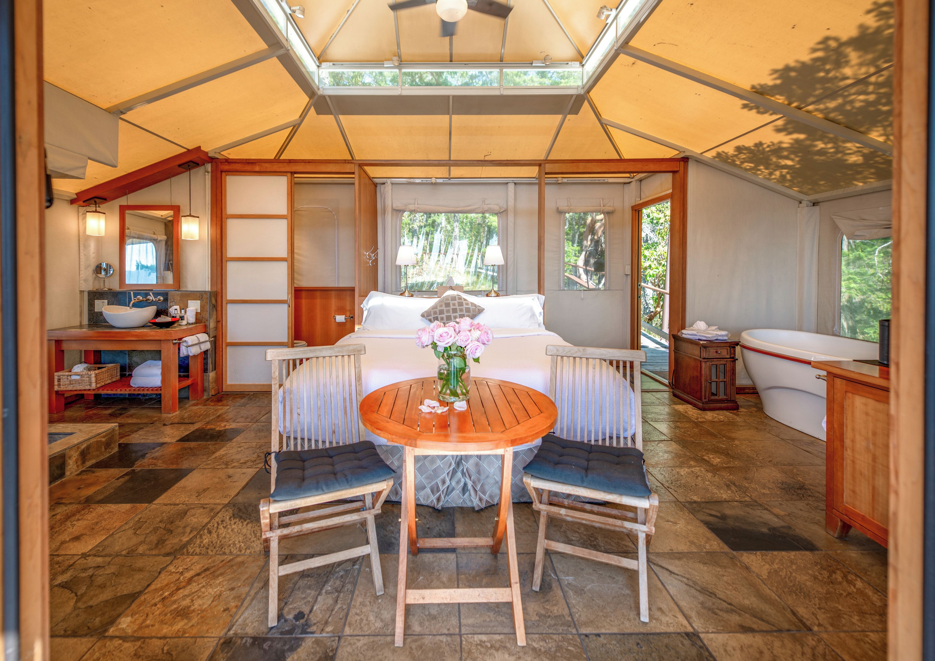 A tented accommodation with a dining area, a bed, and a bathroom.