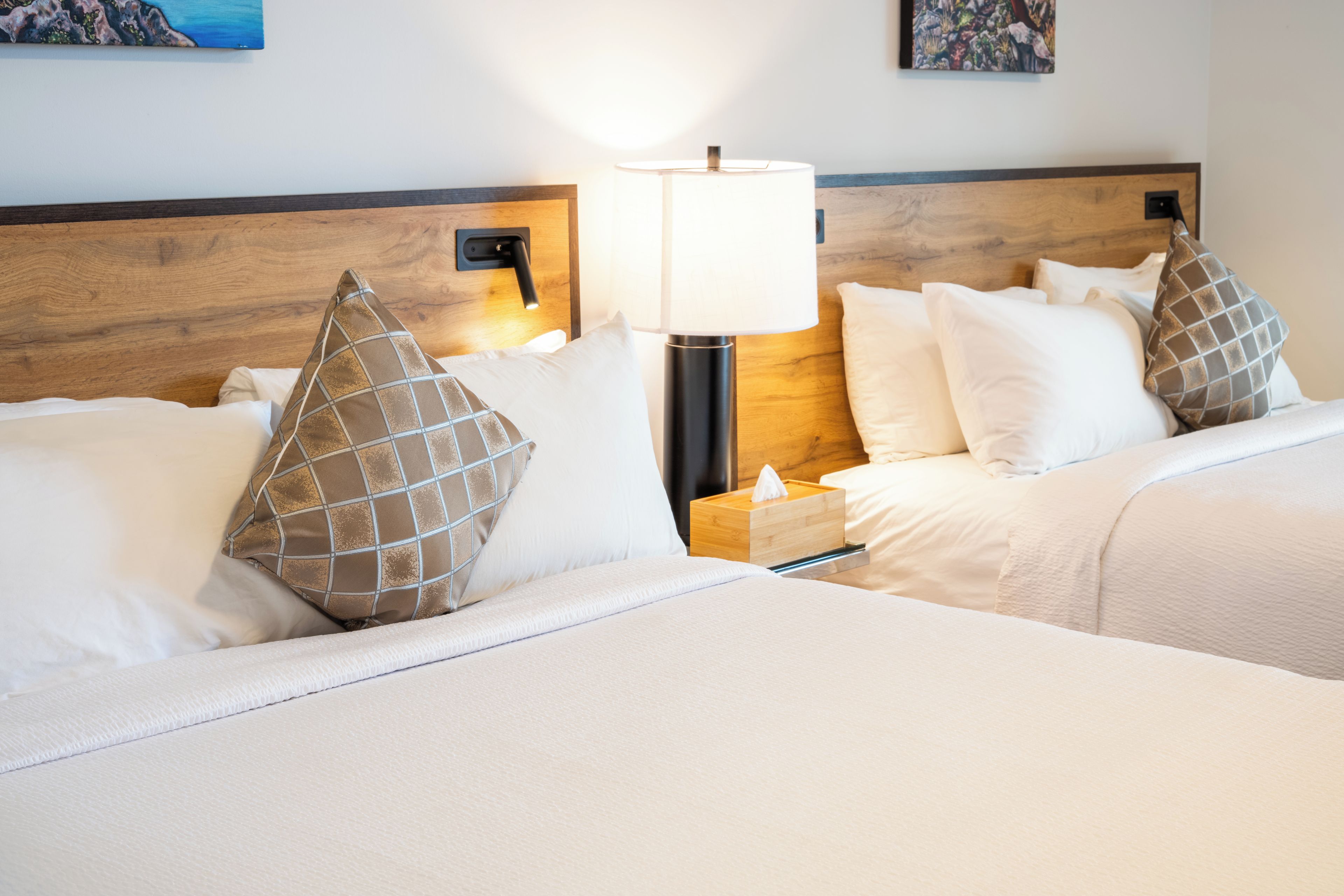 A hotel room with two beds, a bedside lamp, and a wooden headboard.