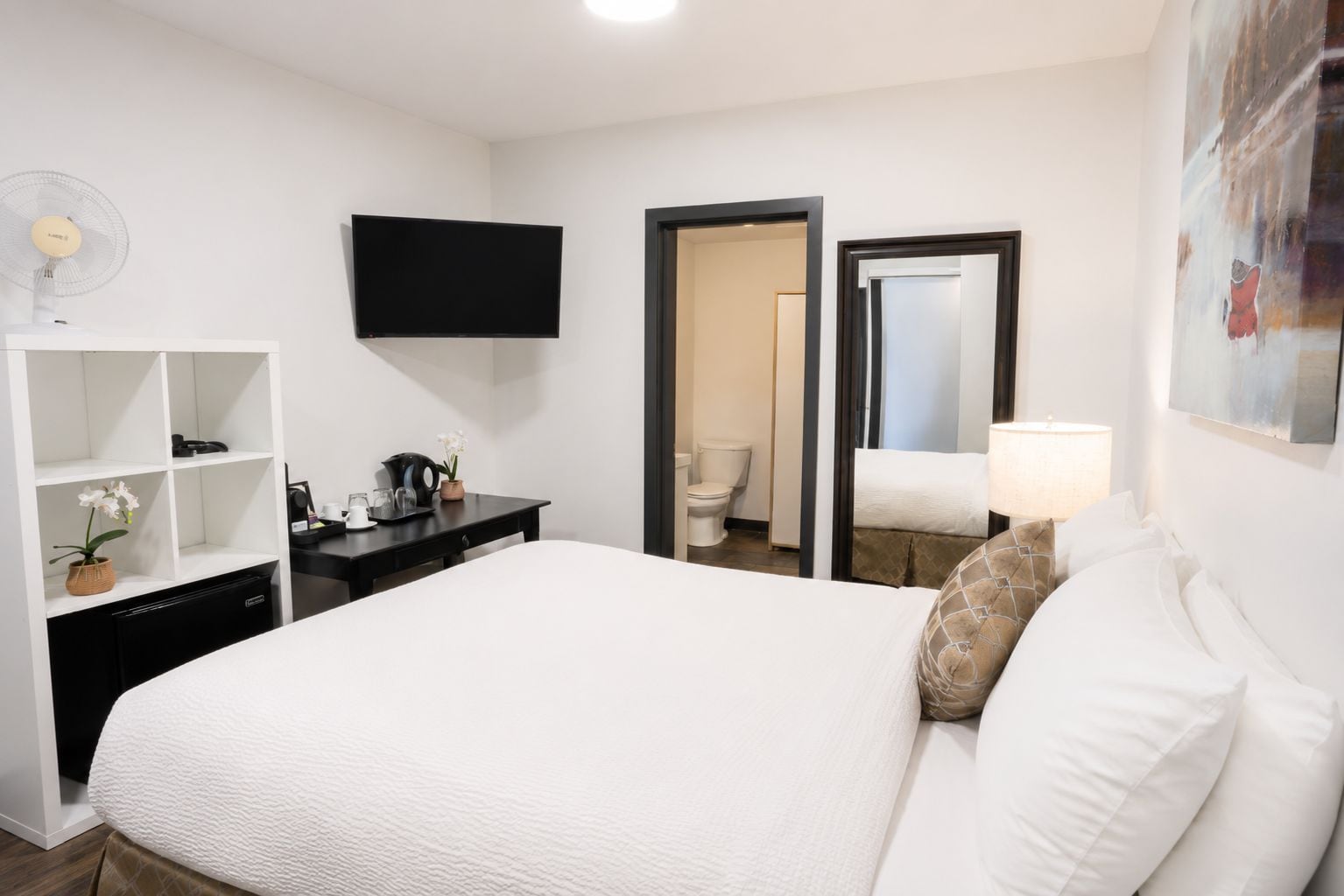 Une chambre d’hôtel équipée d’un lit, d’un bureau, d’une télévision, d’un miroir et d’une porte donnant accès à une salle de bain.