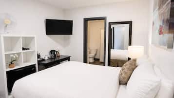 Une chambre d’hôtel équipée d’un lit, d’un bureau, d’une télévision, d’un miroir et d’une porte donnant accès à une salle de bain.