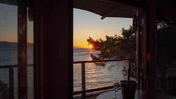 A sunset view from a room with a wooden deck, a glass door, and a table with a wine glass.