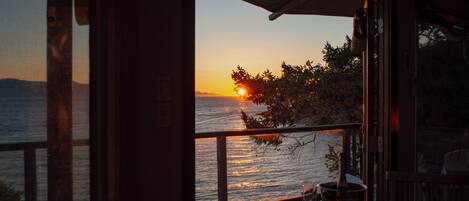 A sunset view from a room with a wooden deck, a glass door, and a table with a wine glass.