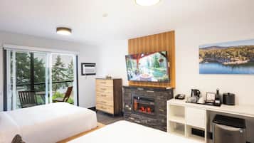 A modern hotel room with a large TV, a fireplace, and a balcony with a view of trees and water.
