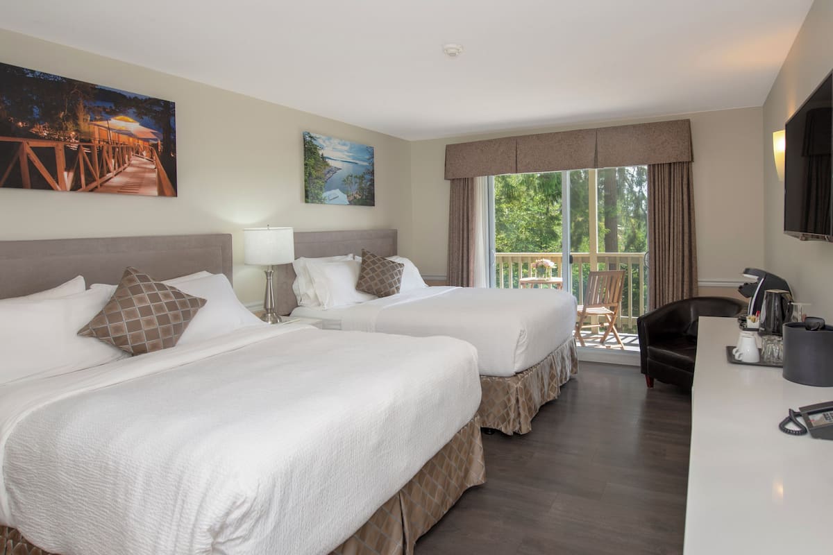 Quarto de hotel com duas camas, uma escrivaninha com cafeteira e uma varanda com vista para árvores.