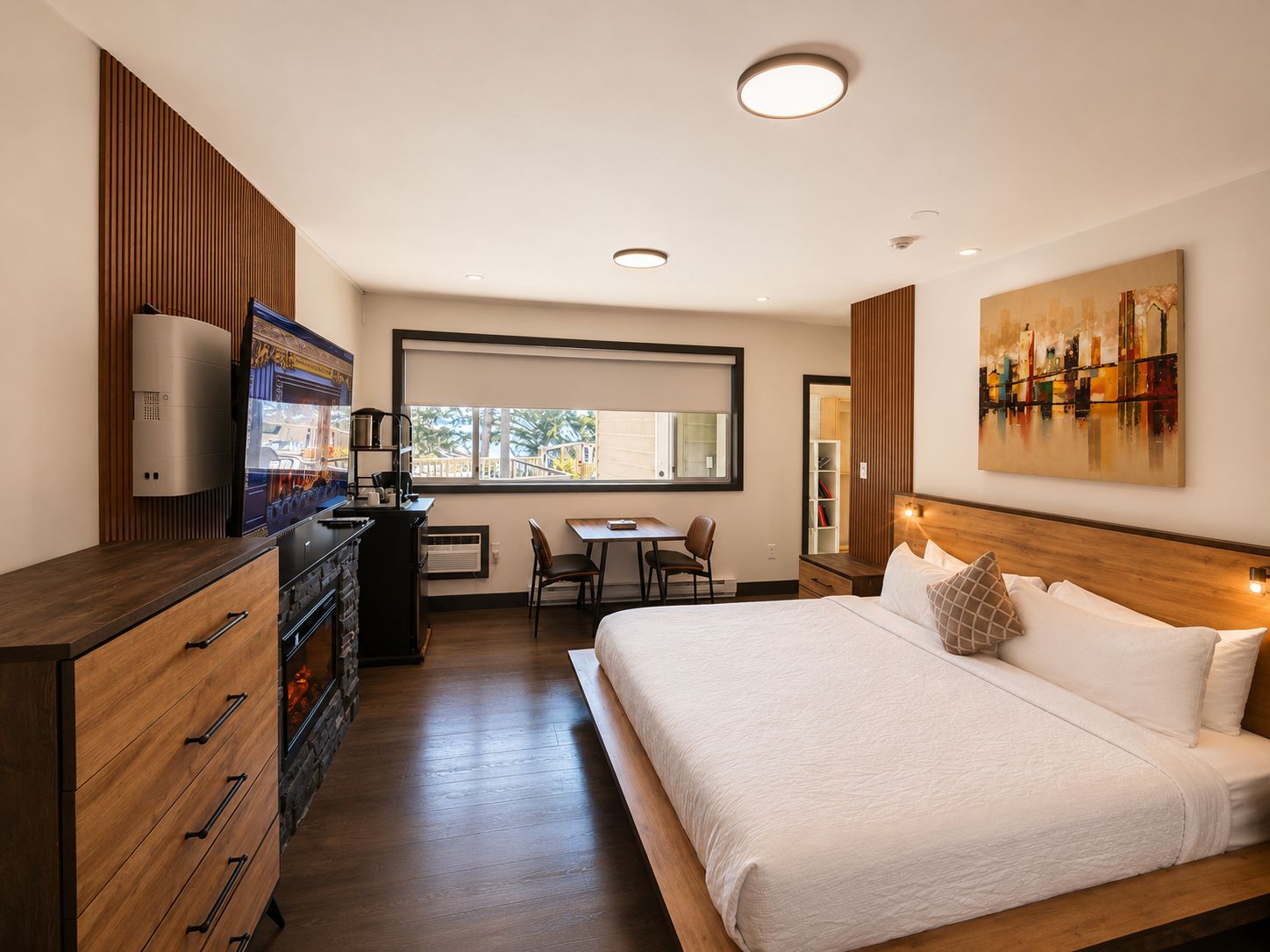 Una habitación de hotel con una cama, un escritorio, una silla, un aparador y un ventanal grande.