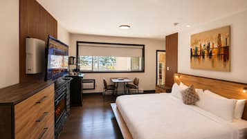 A hotel room with a bed, a desk, a chair, a dresser, and a large window.