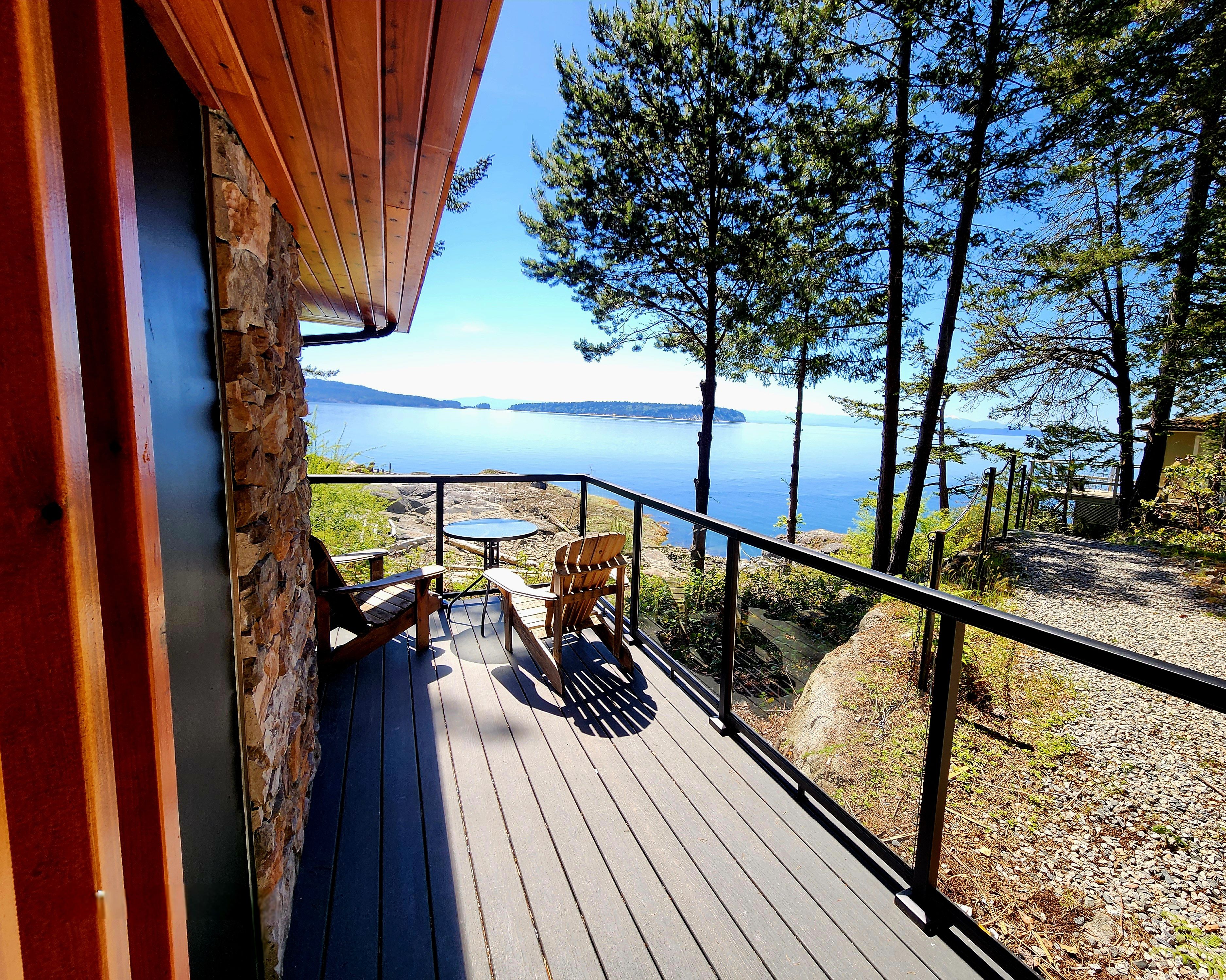 A wooden deck with two chairs and a table, overlooking a body of water and a forested landscape.