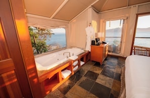 A bathroom with a large bathtub, a wooden vanity, and a view of the sea.