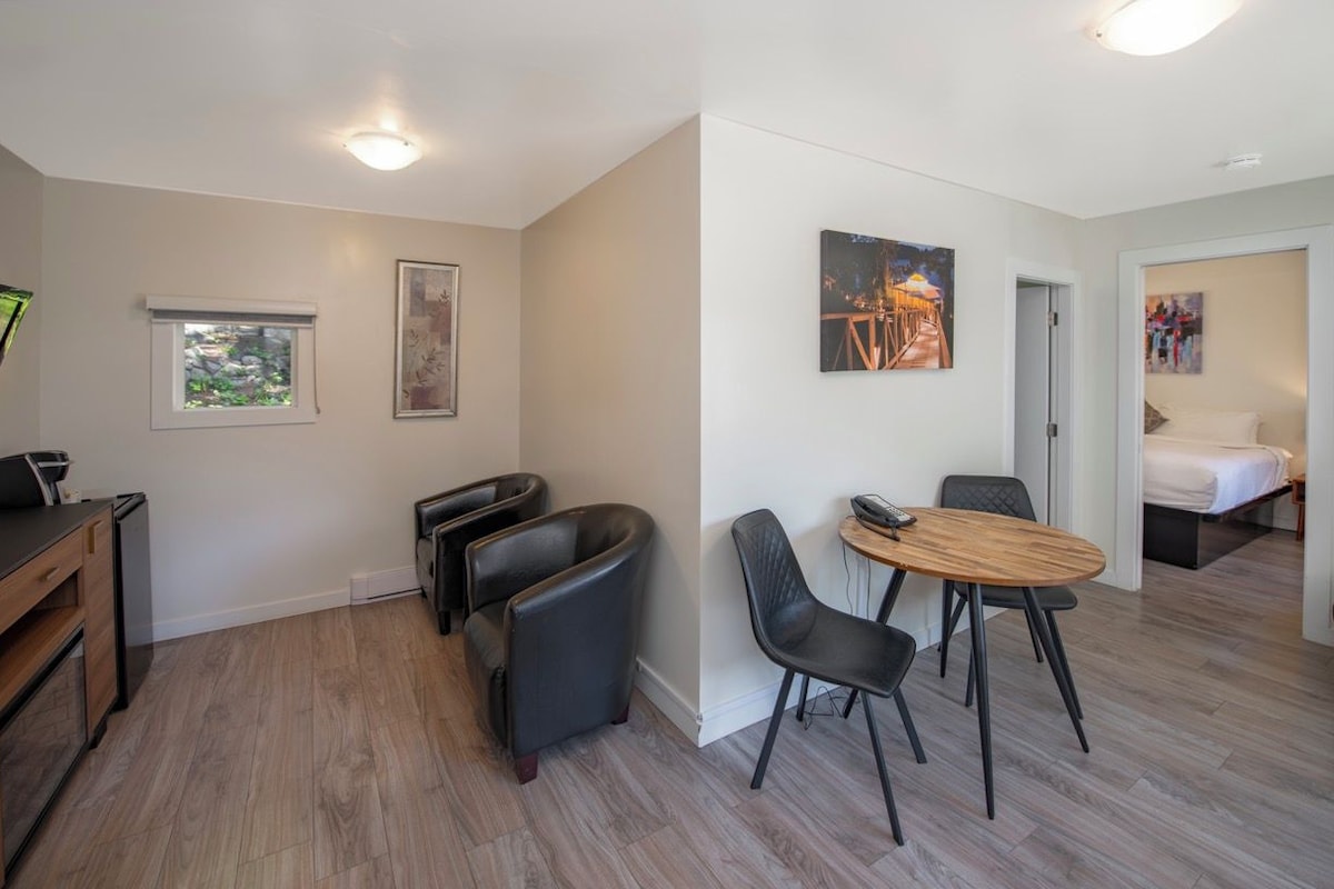 A modern, well-lit room with a dining area, a small kitchen, and a bed.
