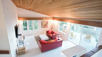 Una sala de estar moderna con un sofá rojo, una mesa de centro blanca y un televisor. Hay ventanas amplias y un balcón con mobiliario exterior.