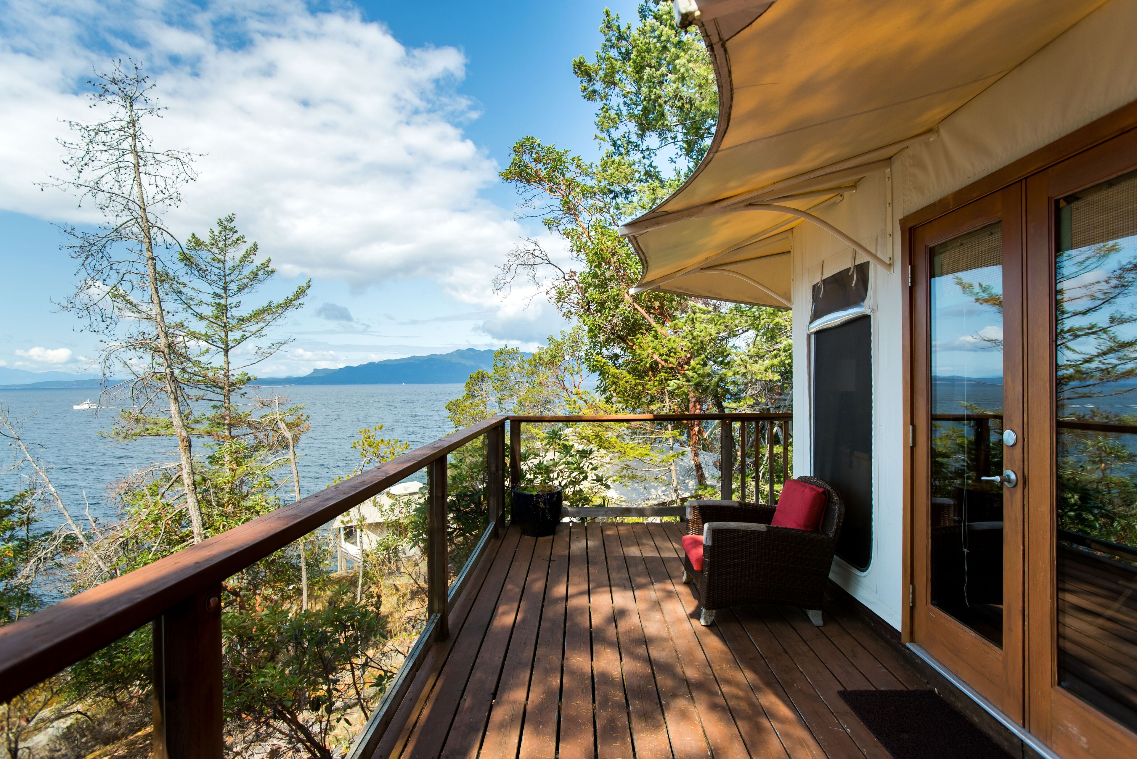 A wooden deck with a view of the sea and mountains, a wicker chair, and a door with glass panels.