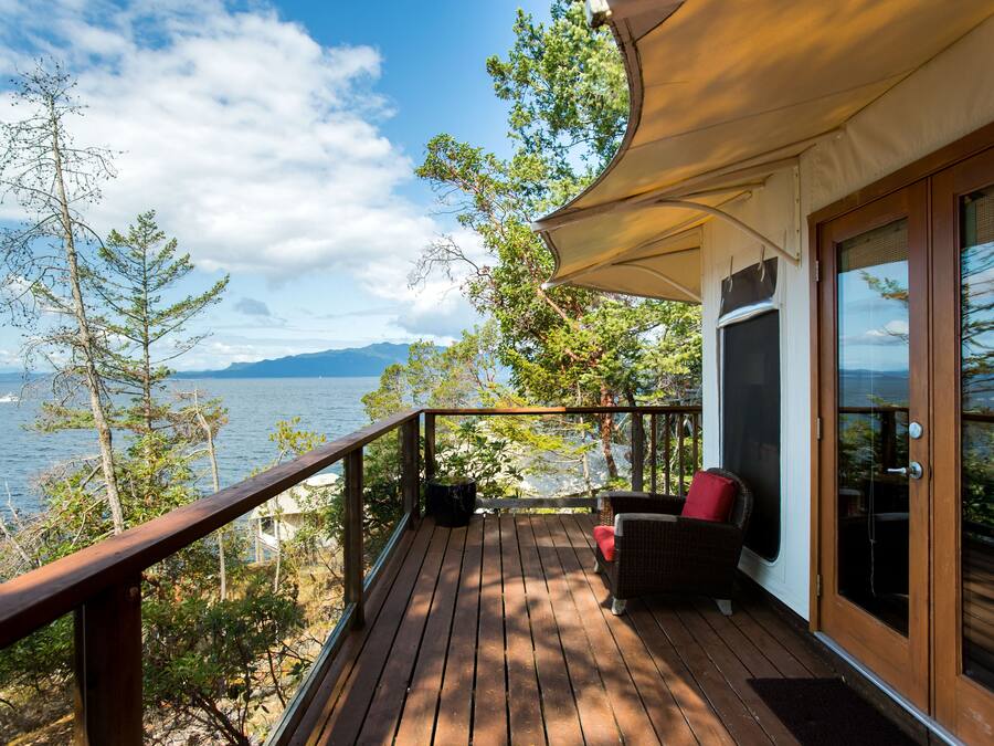 A wooden deck with a view of the sea and mountains, a wicker chair, and a door with glass panels.