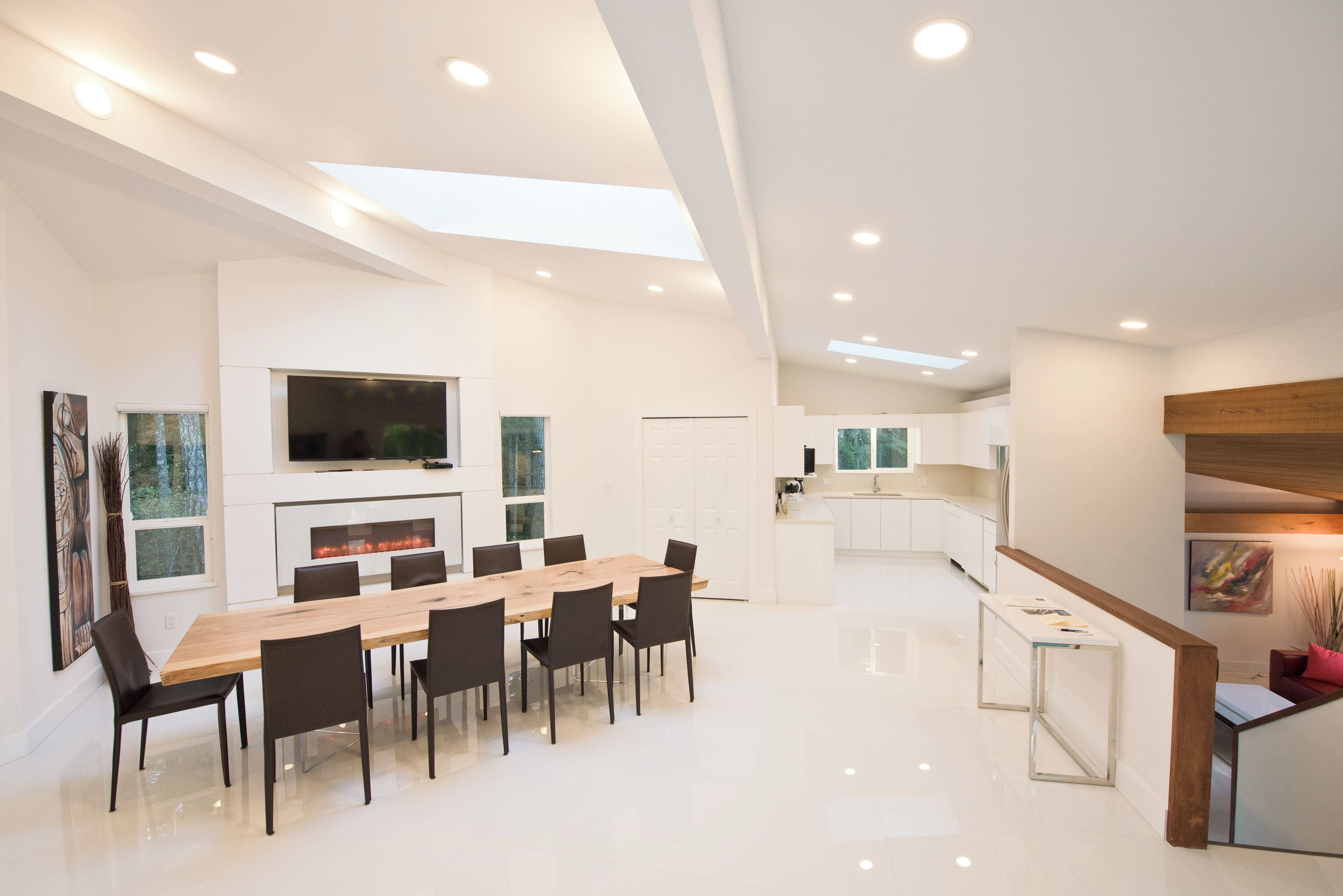 A spacious, modern kitchen with white cabinetry, a central island, and a dining area with a long wooden table and chairs.