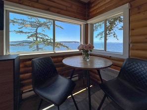 A wooden cabin room with two black chairs, a round table, and a vase of flowers. - Rockwater Secret Cove Resort (Halfmoon Bay)