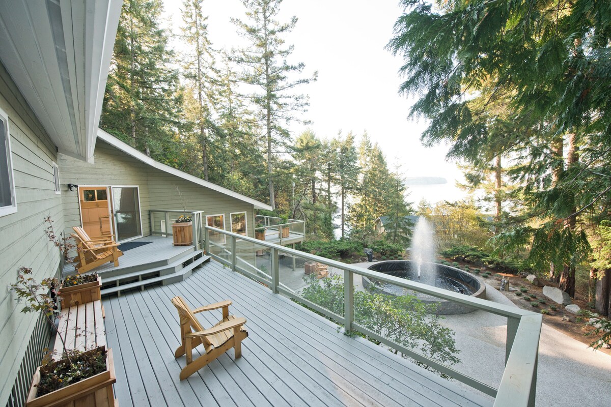 A wooden deck with outdoor seating, a fire pit, and a view of a forested area.