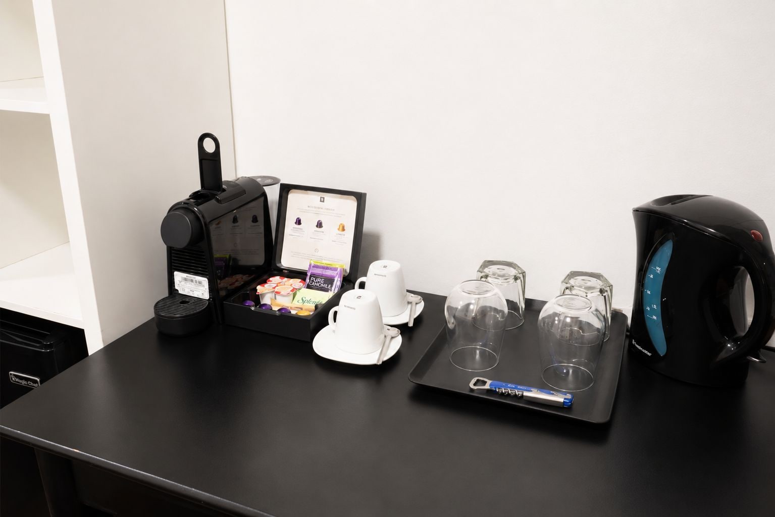 A coffee machine, a tea kettle, and a tray with cups and a teapot on a table.
