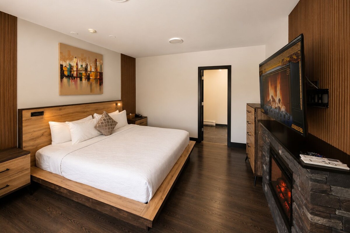 A modern bedroom with a wooden bed, a nightstand, a dresser, and a fireplace.