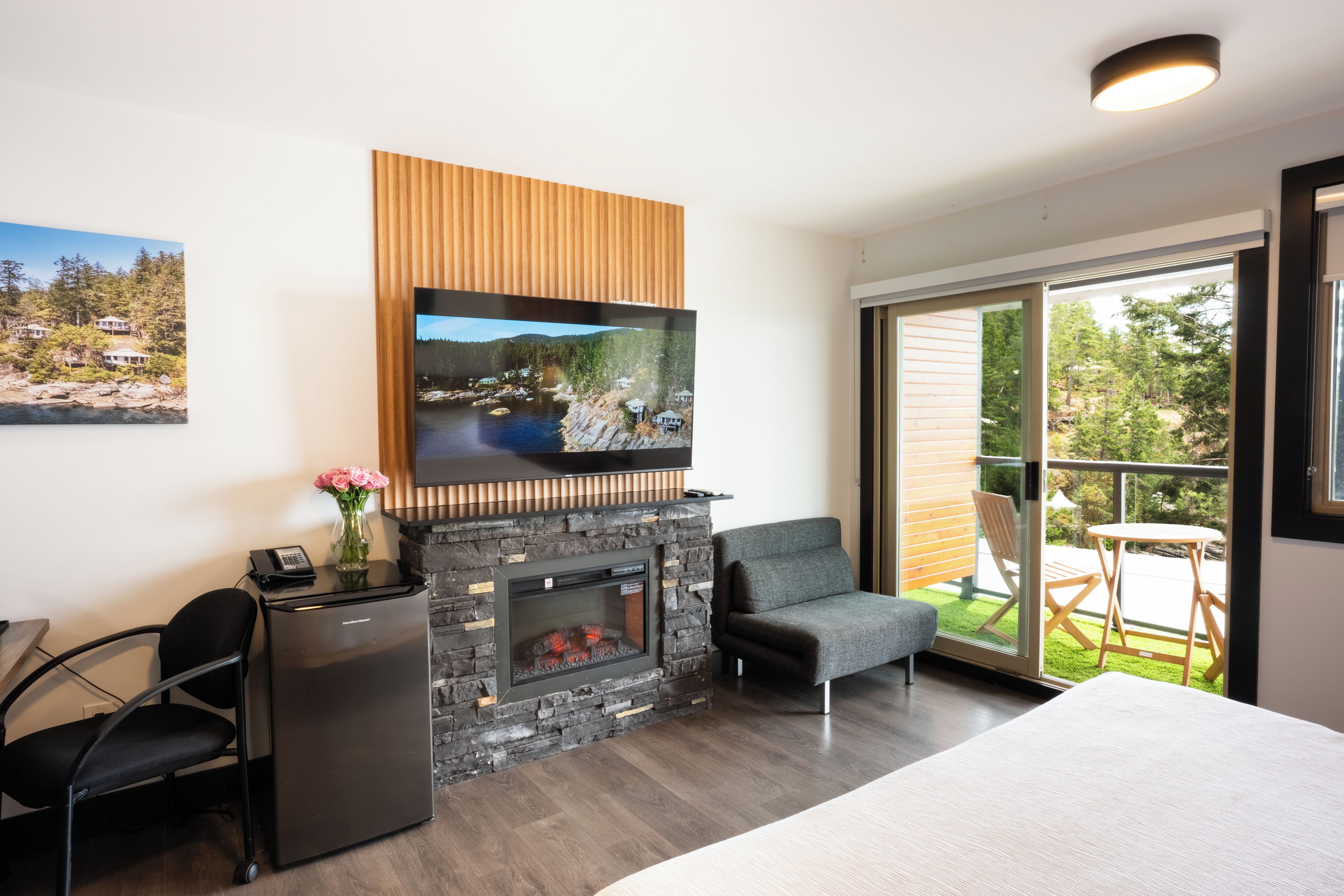 A modern room with a fireplace, a flat-screen TV mounted above it, a desk with a phone, a chair, and a bed.
