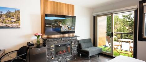 A modern room with a fireplace, a flat-screen TV mounted above it, a desk with a phone, a chair, and a bed.