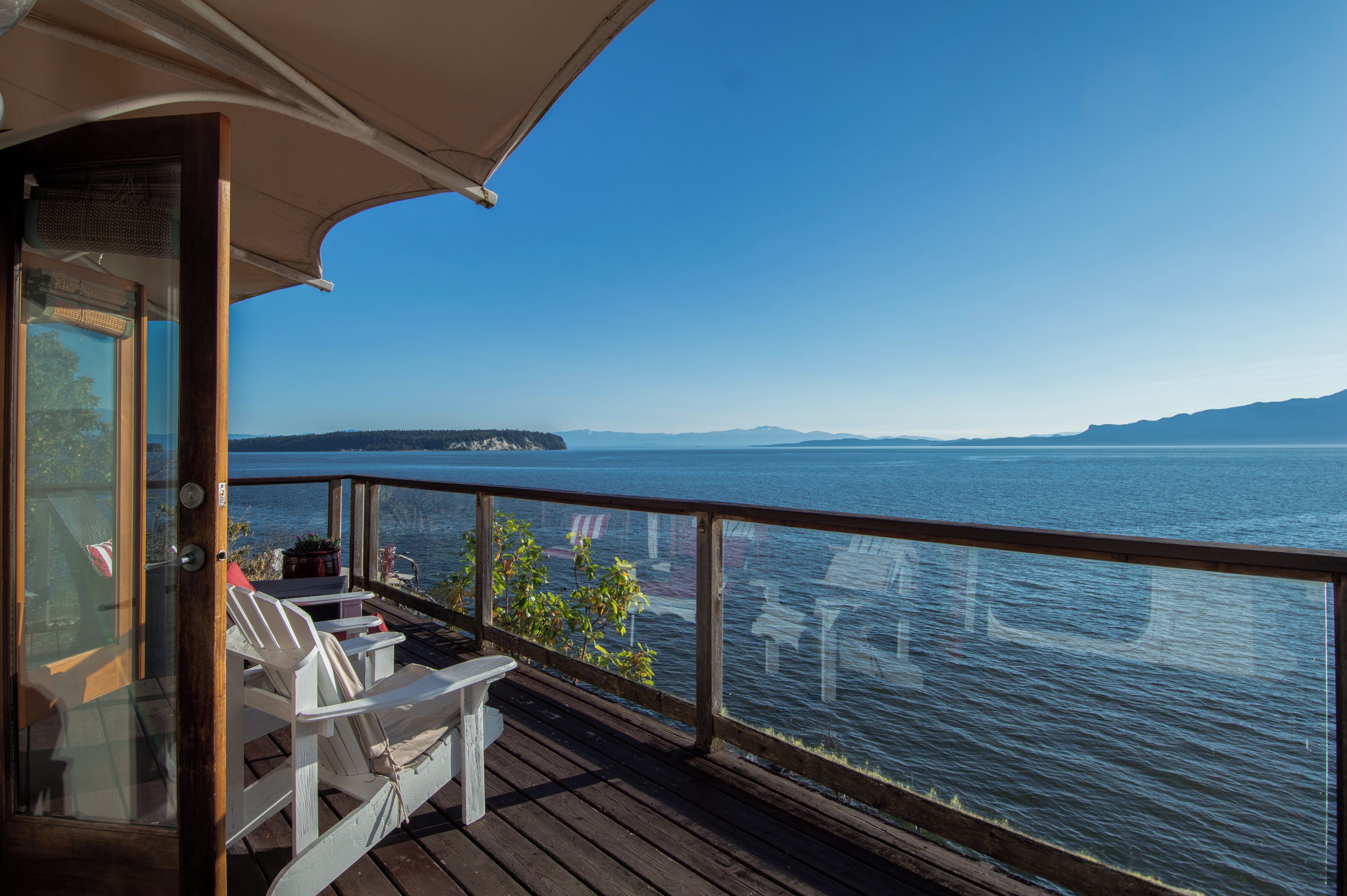 A wooden deck with white chairs and a table, overlooking a large body of water with a distant landmass.