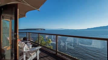A wooden deck with white chairs and a table, overlooking a large body of water with a distant landmass.