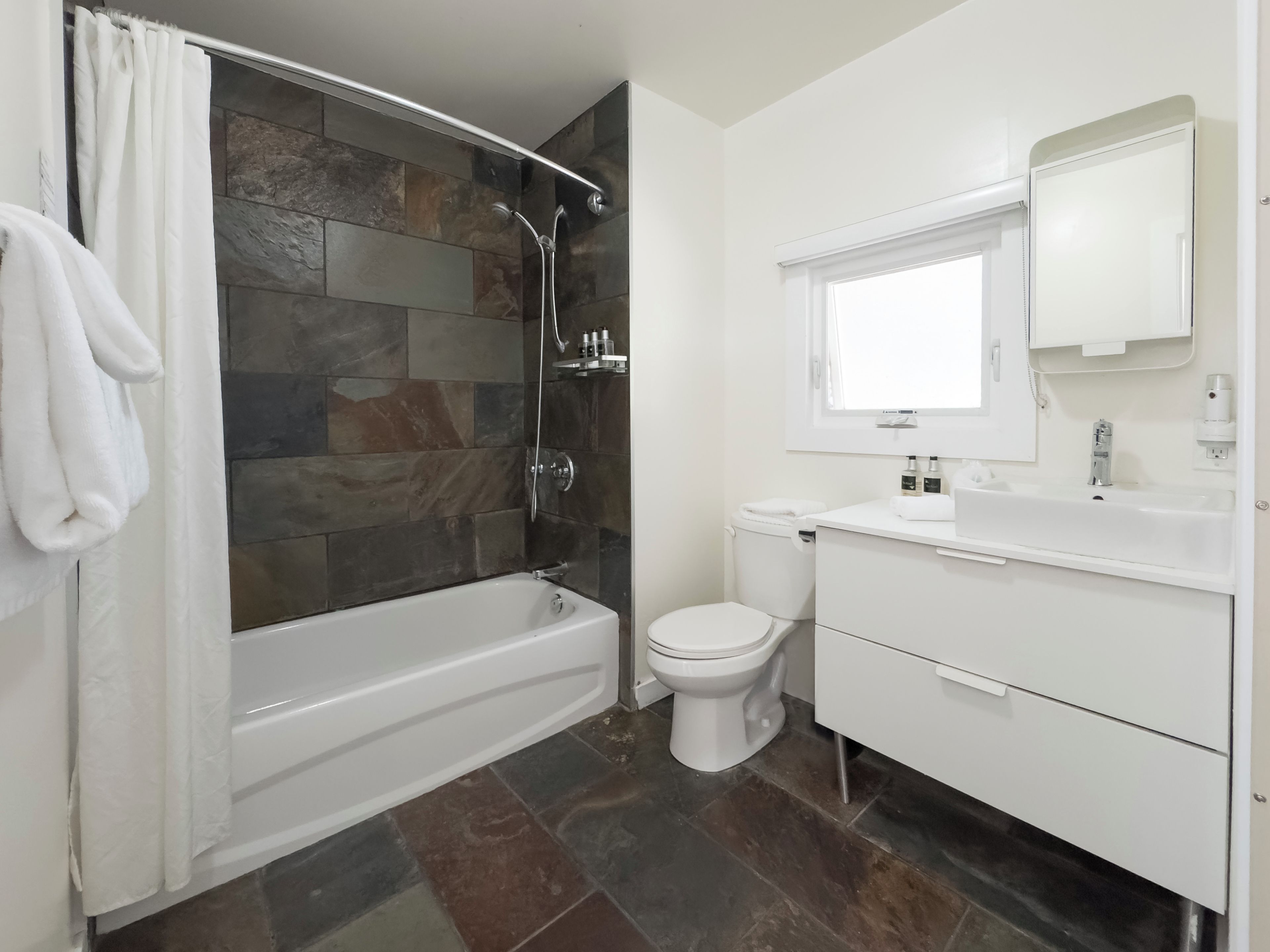 Un baño moderno con ducha de piedra, inodoro y lavabo con espejo.