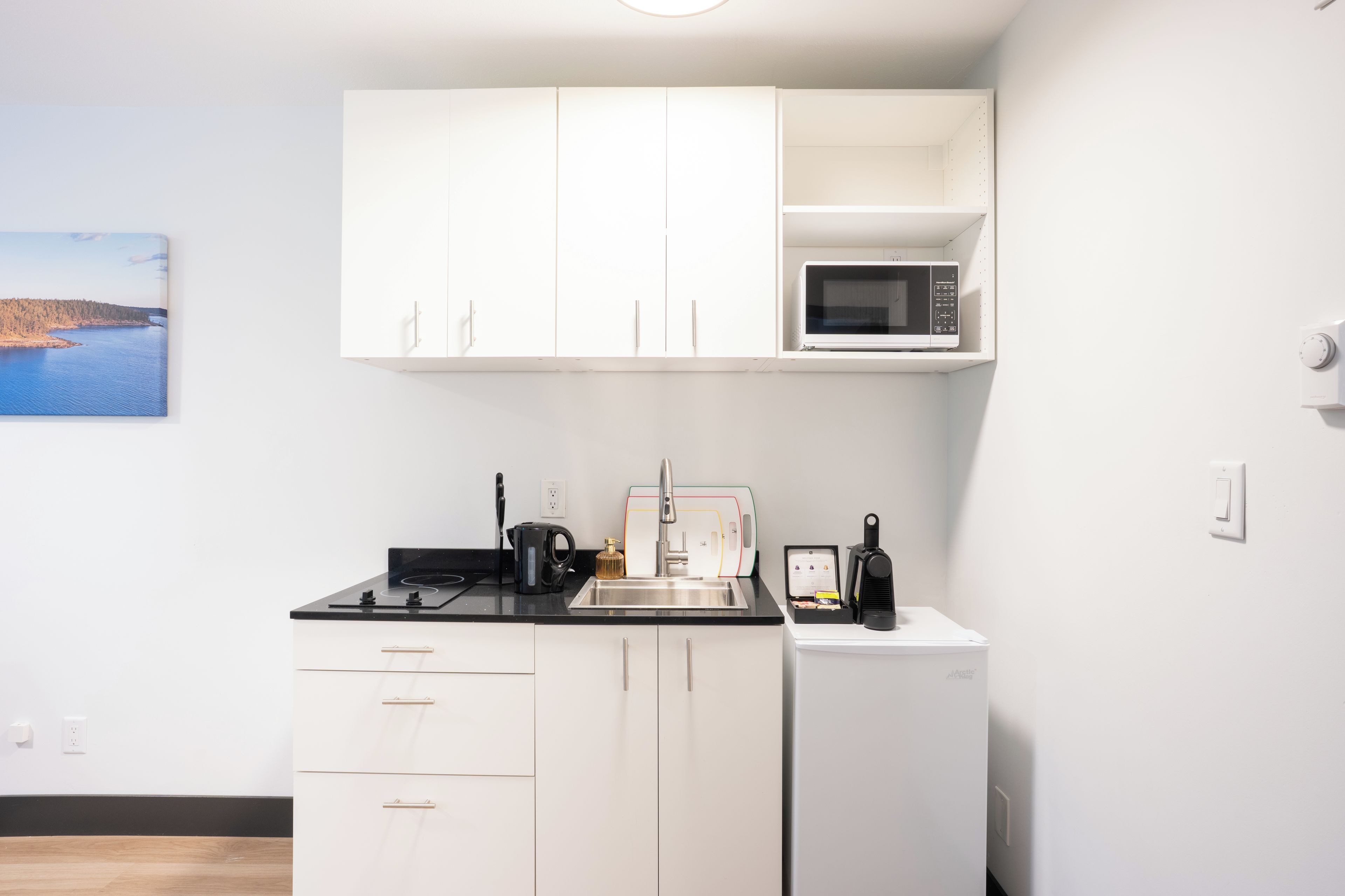 Una kitchenette compacta con armarios blancos, un microondas, una cafetera y un refrigerador pequeño.