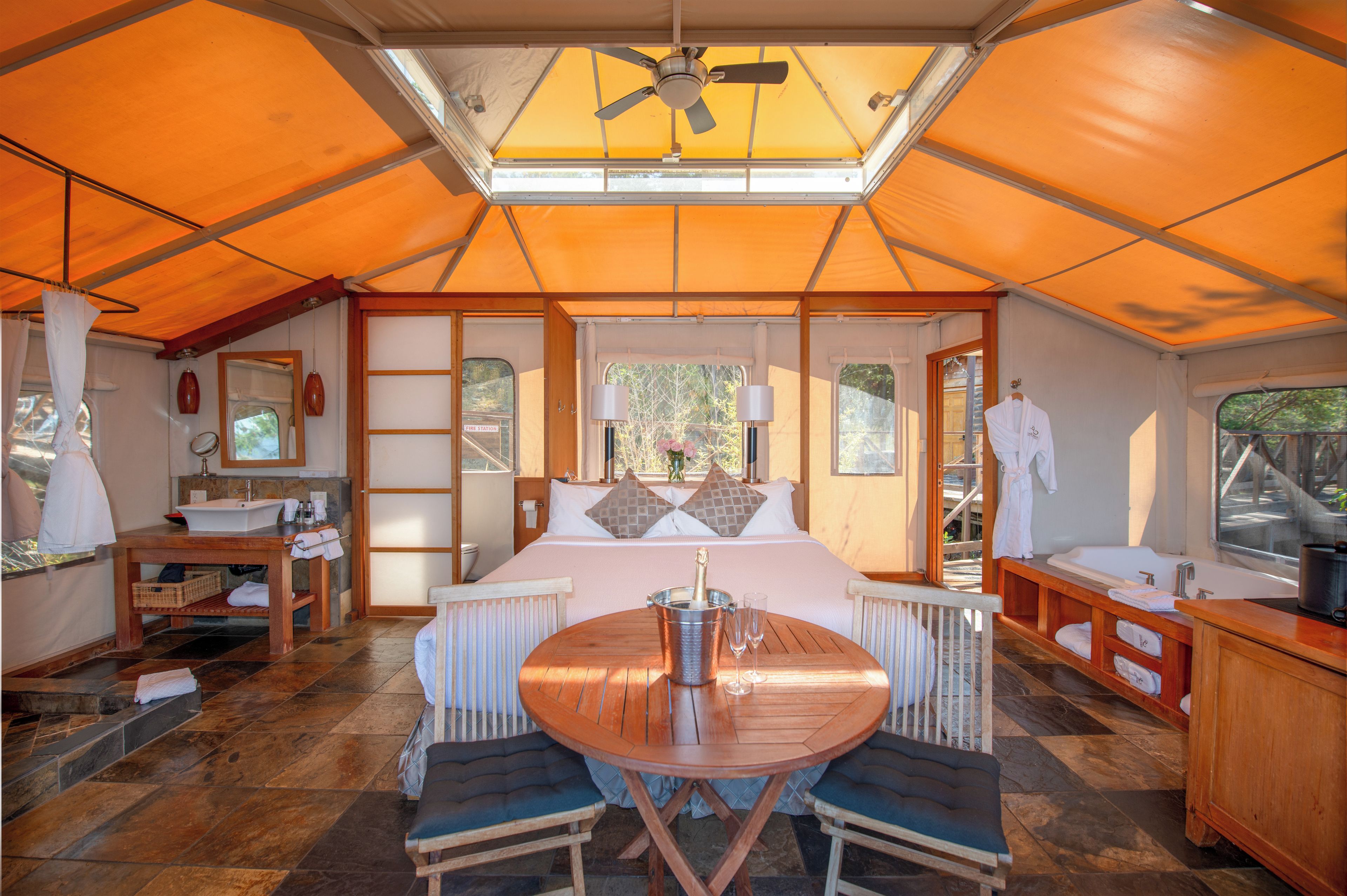 Alojamiento con tienda de campaña, cama, mesa con sillas, lavabo y ventana.