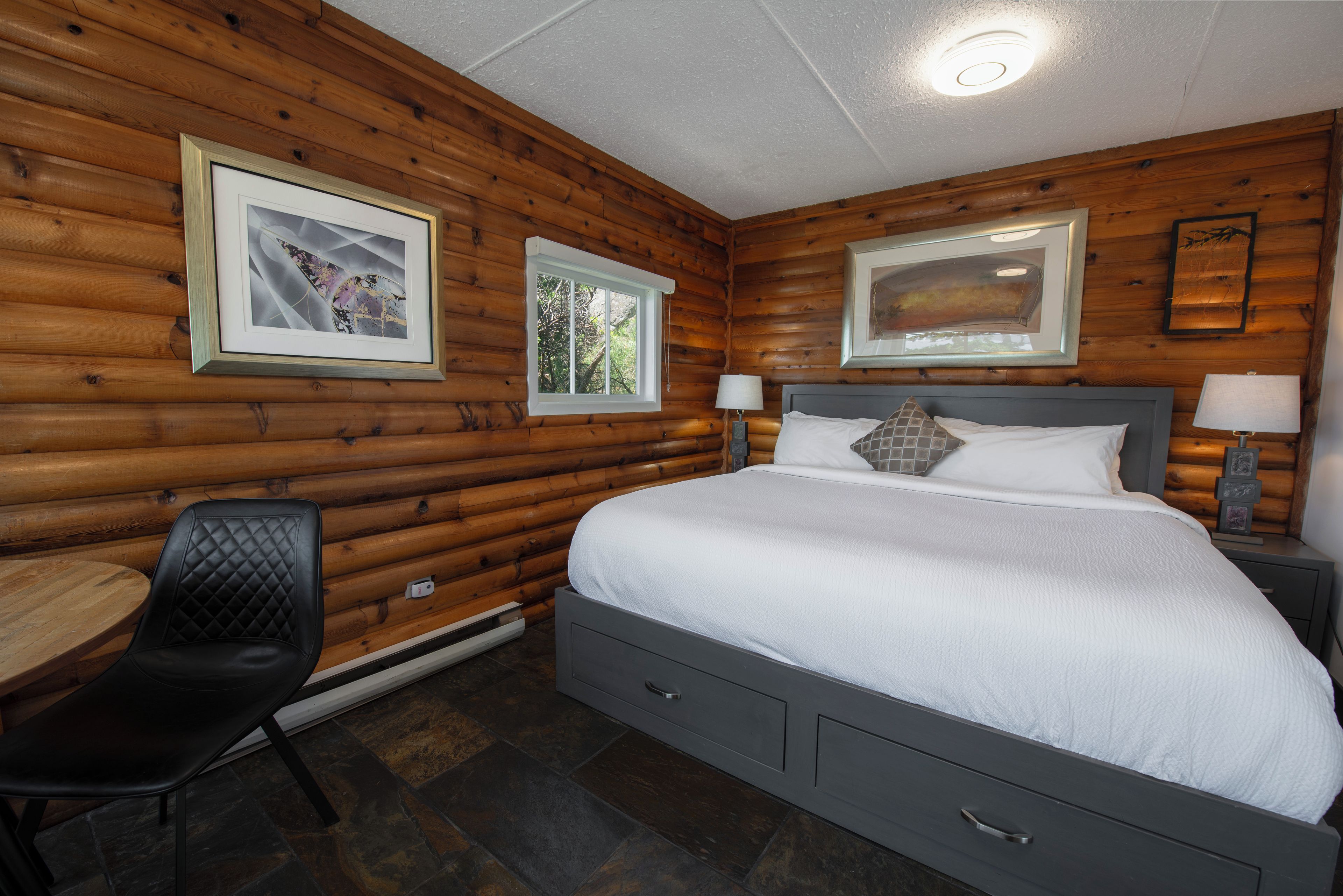 A bedroom with a bed, a chair, a desk, and two framed pictures on the wall.