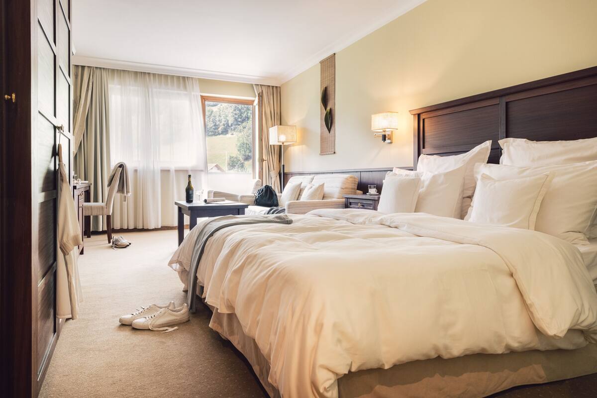 A hotel room with a large bed, a desk, a chair, and a window with curtains.