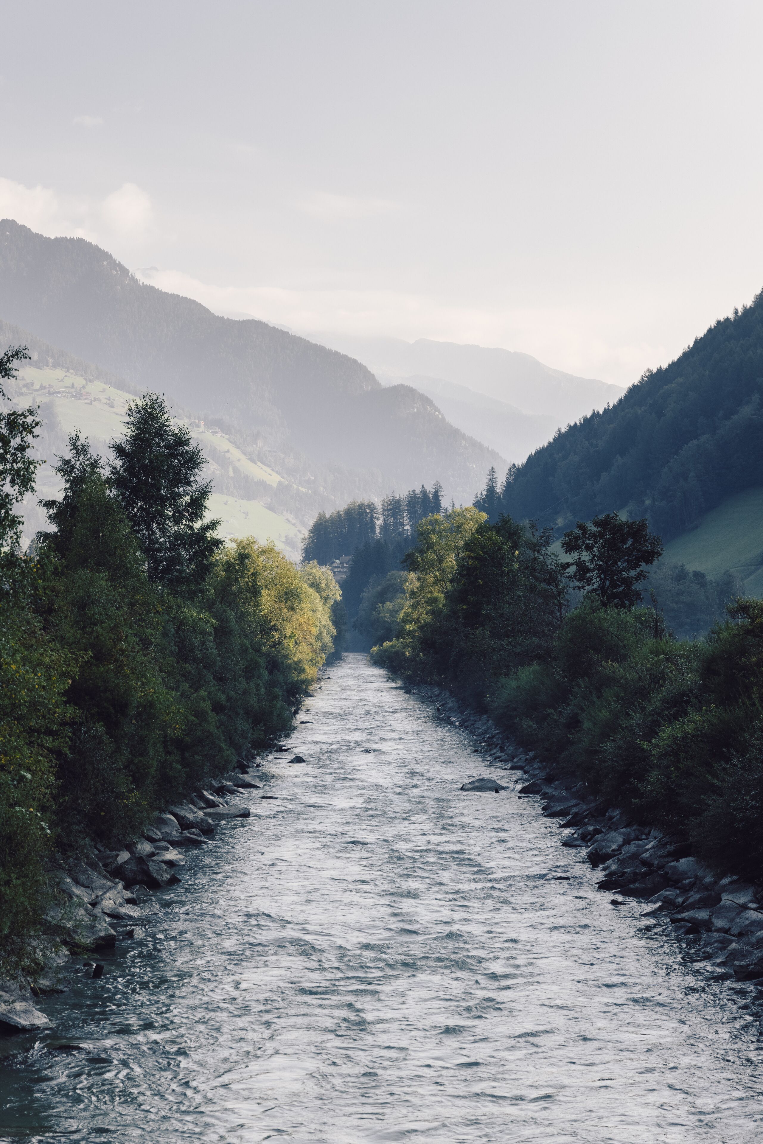 Ein Fluss, der durch ein Tal mit dichter Vegetation und Hügeln im Hintergrund fließt.