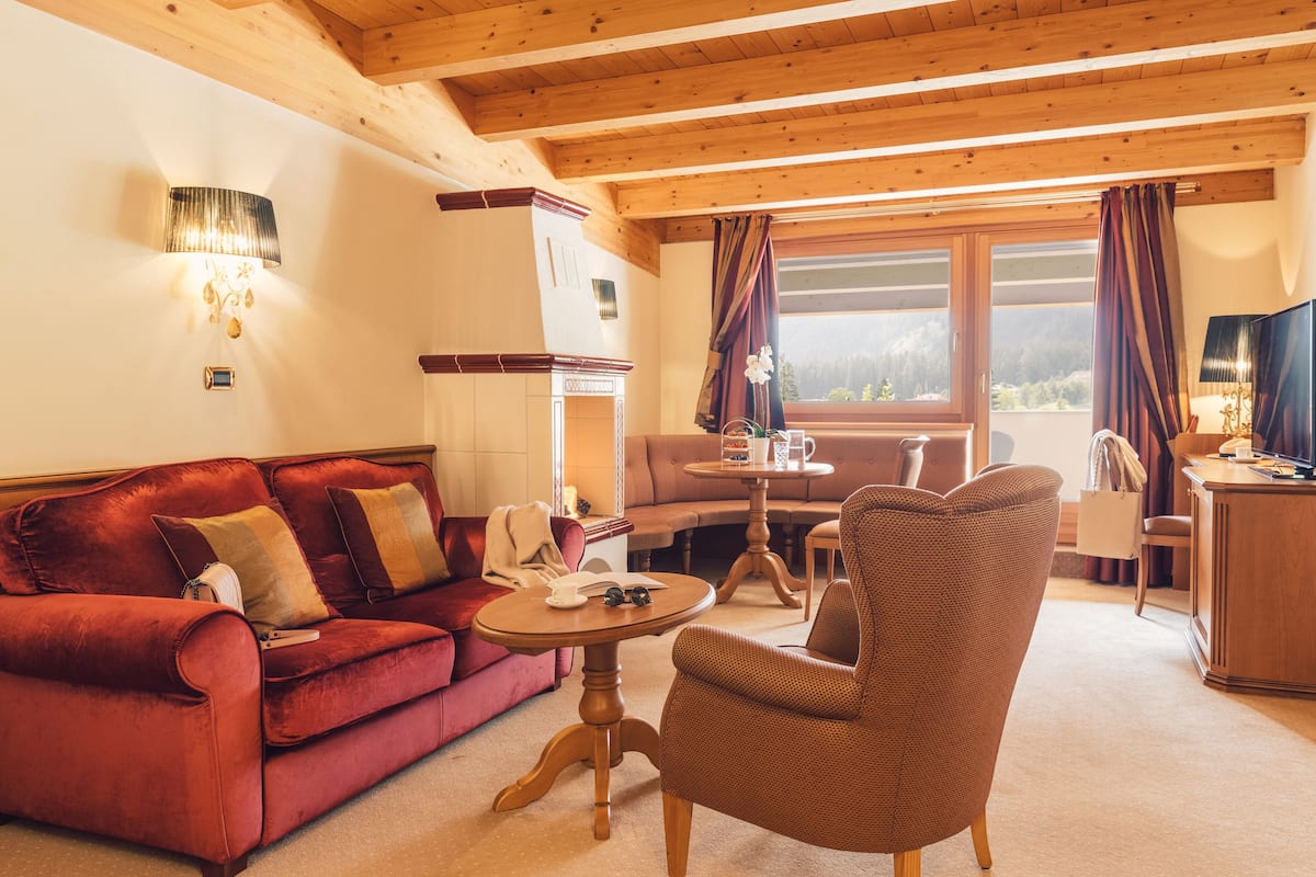 A cozy room with a red sofa, a brown armchair, a wooden ceiling, and a window with curtains.